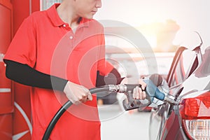 Gas station attendant in red uniform holding a fuel petrol pump nozzle against for filling up the car with petrol at gas station