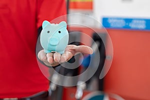 Gas station staff worker with piggy bank for save money from low fuel price, gas costs reduction, cut and saving gasoline drop