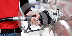 Gas station worker in red uniform filling up bronze pickup truck tank. Closeup hand holding black gas pump nozzle