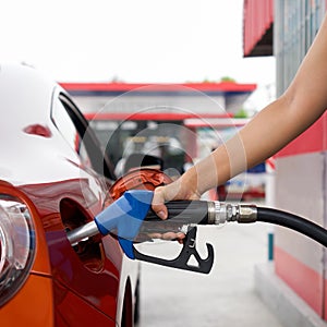 Gas station worker`s hand holding blue benzene gas pump, filling up red sport car tank. Close up