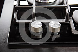 Gas stove burner knobs with black mirror surface of cooker and stainless steel grills. Top view, close up