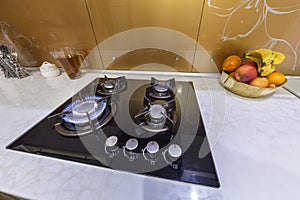 Gas stove flame burner close-up, bowl with fruit on marble counter. Luxury modern fitted kitchen with all appliances interior and