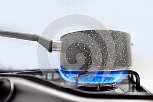 Gas stove with an open blue flame, cook on it dish in ladle