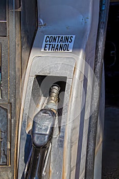 Gasoline fuel pump nozzle  in USA - old and bend and grungy with sign Contains Ethanol and warming message on pump handle