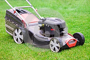 Gasoline lawn mower black and red with grass container on green grass background