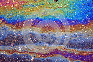 Gasoline spreads over the wet asphalt in the form of a multi-colored large spot