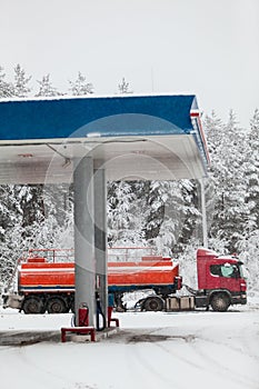 Gasoline tank truck semitrailer draining on gas in station with strong snowfall at winter season