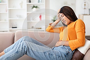Young chinese woman suffering from stomachache, home interior