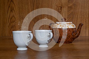 Gastronomic composition with classic cups of hot tea with teapot in the background on wooden table