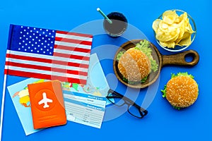 Gastronomical tourism with american flag, passport, tickets, map, burgers, chips, drink on blue background top view