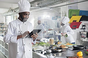 Gastronomy expert with handheld device standing in restaurant professional kitchen while looking for dinner recipes.