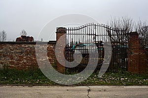 Gate in a brick boundary wall at the edge of a road with building equipments behind the grating in the italian countryside