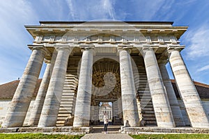 Gate of the building in the Saline Royale Royal Saltworks, with a woman standing under the columns at Arc-et-Senans, France