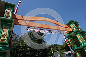 A gate at the entrance of a village has a red and white flag umbul umbul attached which is the Indonesian flag