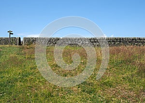 Gate in a long stone wall with a wooden signpost pointing out directions in a green field with blue summer sky