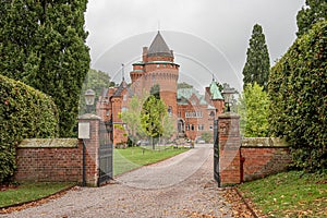 The gate to a romantick red castle inside a park on a green lawn