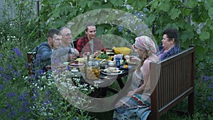 Gathered together relatives and friends at picnic outdoor. Young and elderly relatives eating and drinking at dining table on cour