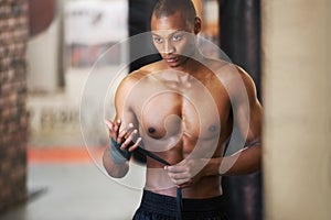 Gathering his thoughts and steeling his mind. An african american boxer taping up his hands at the gym.