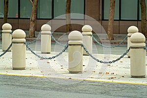Gaurd rails in road or in courtyard with metal chains and cement posts in late afternoon sun in urban area and road photo