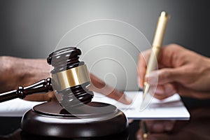 Gavel In Front Of Person`s Hand Signing Legal Document