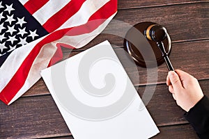 Gavel in judges hand, American flag, blank list on wooden table. Law and justice concept