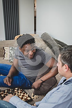 A gay couple enjoying time indoors at home, playing chess.