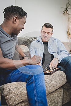 A gay couple enjoying time indoors at home, playing chess.