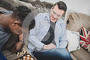A gay couple enjoying time indoors at home, playing chess.