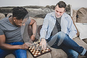 A gay couple enjoying time indoors at home, playing chess.