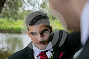 Gay couple of grooms pose for photographs by a lake on their wedding day