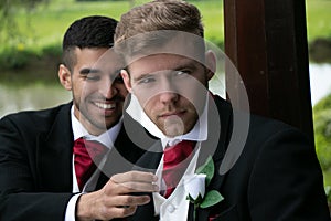 Gay couple of grooms pose for photographs by a lake on their wedding day