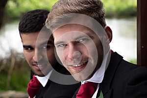 Gay couple of grooms pose for photographs by a lake on their wedding day