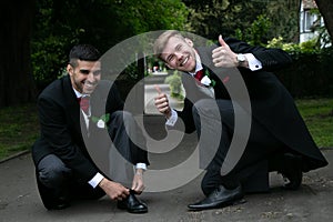Gay couple of grooms pose for photographs whiel tying shoe laces
