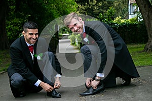 Gay couple of grooms pose for photographs whiel tying shoe laces