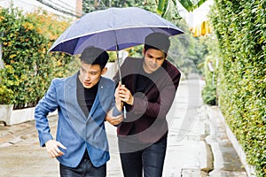 Gay couple holding umbrella and hands together. Asian homosexual men walking in the rain.