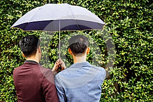 Gay couple holding umbrella and hands together. Back of homosexual men walking in the rain.