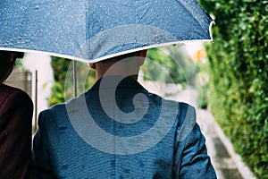 Gay couple holding umbrella and hands together. Back of homosexual men walking in the rain.