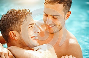 Gay couple relaxing in swimming pool. LGBT. Two young men enjoying nature outdoors, kissing and hugging