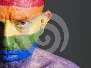 Gay flag painted face man, serious expression.