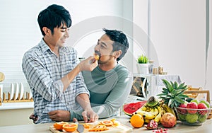 Gay LGBT sweet Asian couple wearing pajamas, smiling with happiness and love, eating, feeding orange, healthy fruits for breakfast