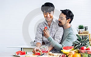 Gay LGBT sweet Asian couple wearing pajamas, smiling with happiness and love, eating, feeding watermalon, healthy fruits for