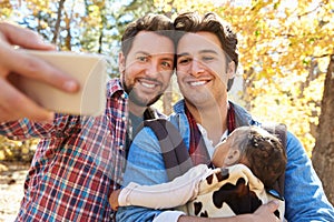 Gay Male Couple With Baby Taking Selfie On Walk In Woodland