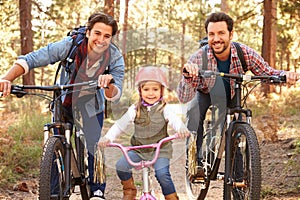 Gay Male Couple With Daughter Cycling Through Fall Woodland