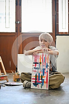 A gay man sitting on the gallery floor with his painted canvas. LGBTQ+ and creative leisurE