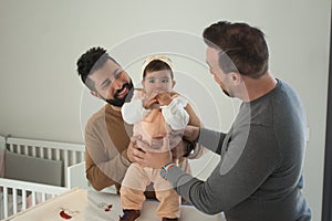 Gay married couple changing their daughterÃÂ´s diaper in the bedroom