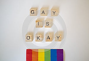 Gay is okay word tiles LGBTQ+ on a white background with a rainbow flag