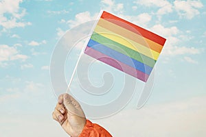 Gay pride rainbow flag fluttering backlit in the sun against soft blue sky