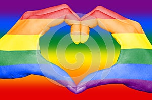 Gay rainbow flag painted on hands forming a heart on rainbow background, gay love concept