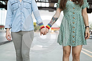Gay women holding hands with rainbow bracelets
