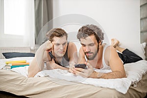 Gays lying on bed with smartphone